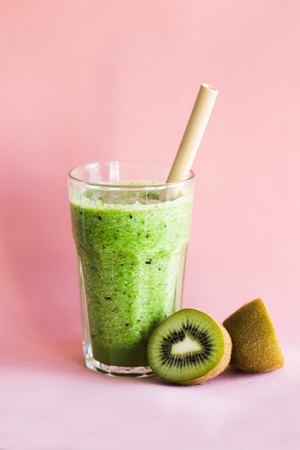 Healthy green smoothie with kiwi and spinach in a glass Cup on a pink backgroundの写真素材