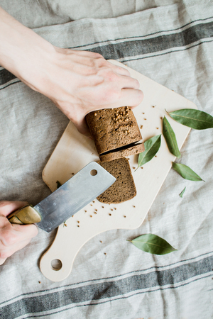 cutting with a knife freshly baked bread on a wooden Board on grey fabric