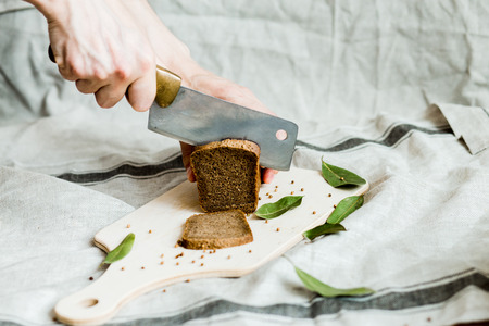 cutting with a knife freshly baked bread on a wooden Board on grey fabric