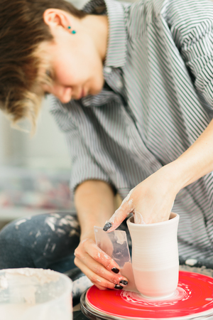 Women working on the potter's wheel. Hands sculpts a cup from clay pot. Workshop on modeling on the potter's wheel.の写真素材