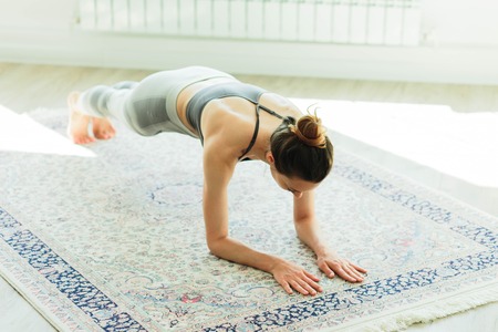 Young attractive smiling woman practicing yoga in a large, bright room