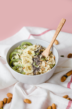 healthy Breakfast of oatmeal with kiwi, banana and chia seed on a white napkin, on pink backgroundの写真素材