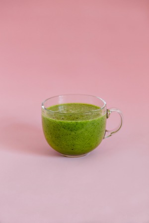 Healthy green smoothie with kiwi and green apple in a glass cup on pink backgroundの写真素材