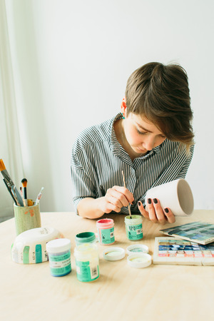 the pottery woman holds in hands a mug to paint the ornament, handmade ceramicの写真素材