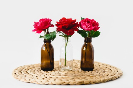 Red roses in glass vases on a nature wicker napkin on white backgroundの写真素材
