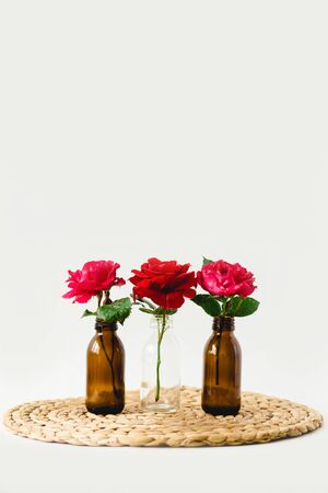 Red roses in glass vases on a nature wicker napkin on white backgroundの写真素材