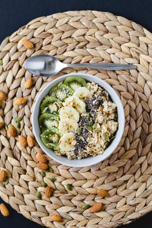 healthy Breakfast of oatmeal with kiwi, banana and chia seed on a wicker napkin, on black backgroundの写真素材