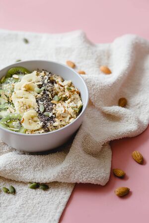 healthy Breakfast of oatmeal with kiwi, banana and chia seed on a white napkin, on pink backgroundの写真素材