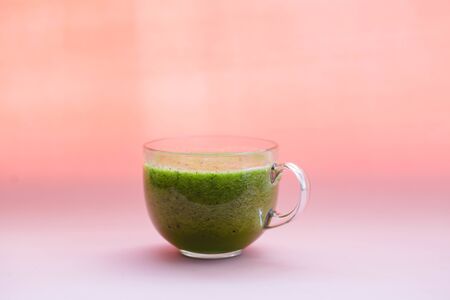 Healthy green smoothie with kiwi and spinach in a glass Cup on a pink background
