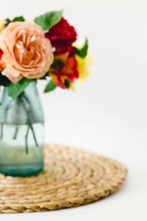 Coloful roses in vase on a nature wicker napkin on white backgroundの写真素材