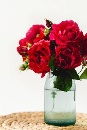 Coloful roses in vase on a nature wicker napkin on white backgroundの写真素材