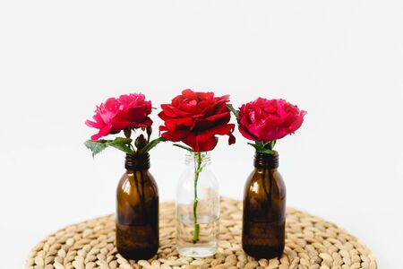 Red roses in glass vases on a nature wicker napkin on white backgroundの写真素材