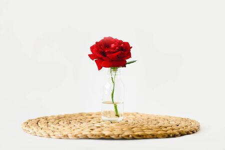 Red roses in glass vases on a nature wicker napkin on white backgroundの写真素材