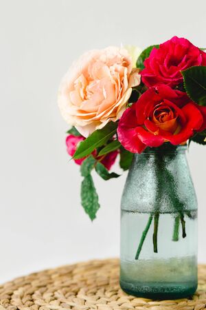 Coloful roses in vase on a nature wicker napkin on white backgroundの写真素材