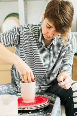 Women working on the potter's wheel. Hands sculpts a cup from clay pot. Workshop on modeling on the...