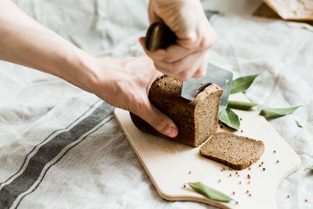 cutting with a knife freshly baked bread on a wooden Board on grey fabric