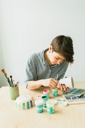the pottery woman holds in hands a mug to paint the ornament, handmade ceramicの写真素材