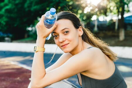 Young woman with a bottle of water after Jogging outdoors in Singapore. She is wearing grey top and...