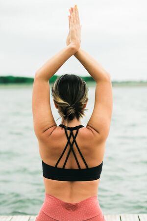 Asian young girl doing yoga outdoors on the pier by the lake. she's wearing a black top and red leggings.の写真素材