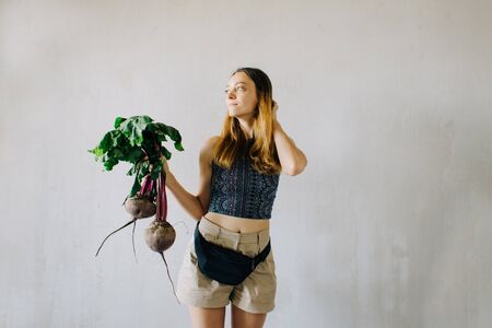 young pretty girl holding fresh organic beet on grey background, summer foodの写真素材