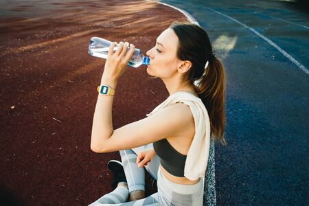 Young woman with a bottle of water after Jogging outdoors in Singapore. She is wearing grey top and a light sports leggingsの写真素材