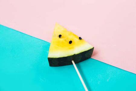 triangular ice cream slices on a stick of ripe yellow watermelon on a blue-pink backgroundの写真素材