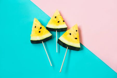triangular ice cream slices on a stick of ripe yellow watermelon on a blue-pink backgroundの写真素材