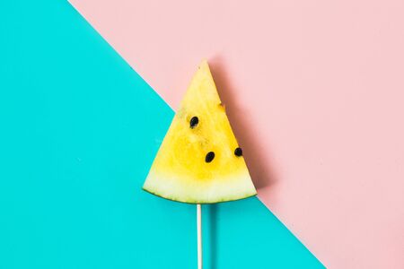 triangular ice cream slices on a stick of ripe yellow watermelon on a blue-pink backgroundの写真素材