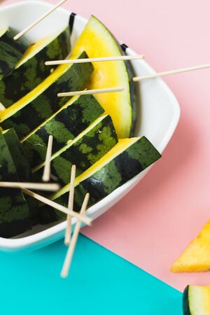 triangular ice cream slices on a stick of ripe yellow watermelon on a blue-pink background