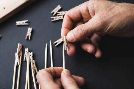 glue together wooden clothespins and sticks, make a holder for photos on a black backgroundの写真素材