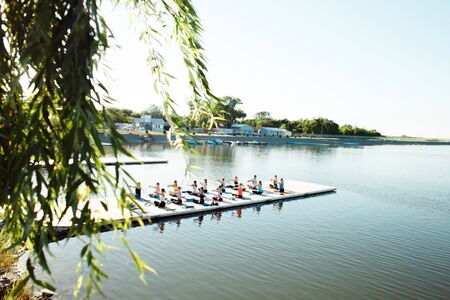 A big group of people attending yoga classes on a pontoon near the lake.の写真素材