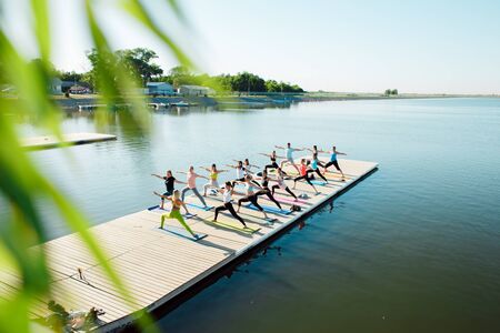 A big group of people attending yoga classes on a pontoon near the lake.の写真素材