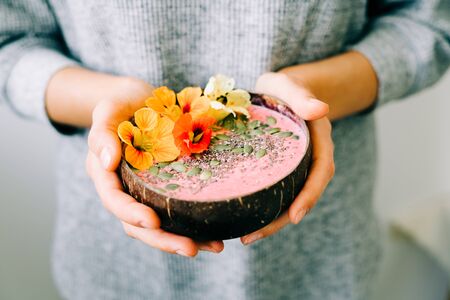 healthy breackfast in bowl of coconut with nasturtium flowers in handsの写真素材