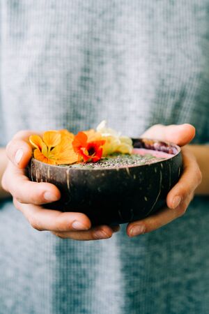 healthy breackfast in bowl of coconut with nasturtium flowers in hands