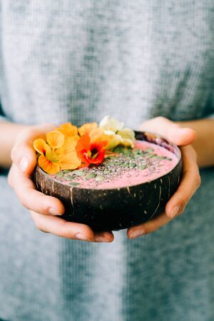 healthy breackfast in bowl of coconut with nasturtium flowers in handsの写真素材