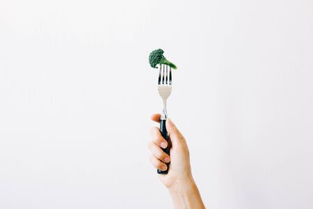 hand holding a fork with a green inflorescence of fresh broccoli on a white background.の写真素材