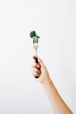 hand holding a fork with a green inflorescence of fresh broccoli on a white background.の写真素材