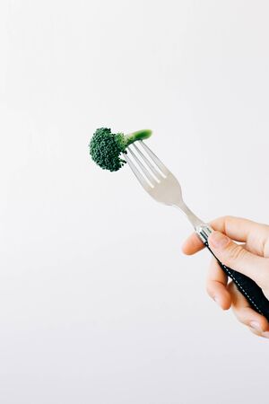 hand holding a fork with a green inflorescence of fresh broccoli on a white background.の写真素材