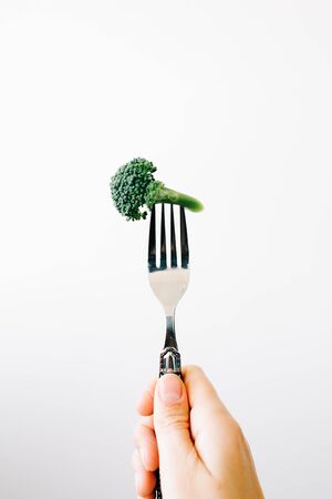 hand holding a fork with a green inflorescence of fresh broccoli on a white background.の写真素材