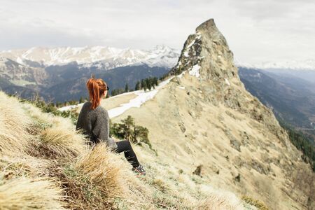 a young girl traveler sits on the grass and looks at the peak of the mountain Zakanの写真素材