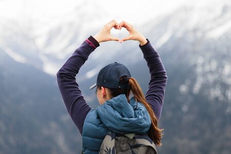a young girl traveler stands on top of a mountain and shows her hands a heart on top of mount Zakanの写真素材
