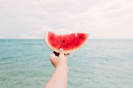 a slice of ripe juicy watermelon in the hands of the sea. on beachの写真素材
