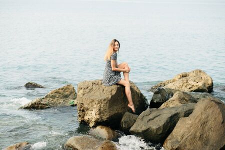 a young girl in a dress on large stones, a picturesque place on the sea coast. summerの写真素材