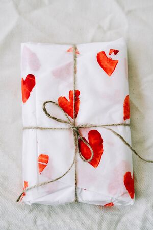 a gift wrapped in homemade wrapping paper with red hearts tied with jute thread for Valentine's day
