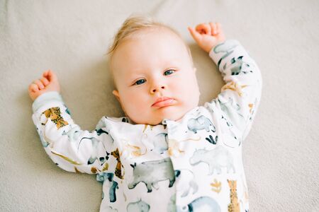 a small beautiful boy in a jumpsuit with animals is lying on the couch