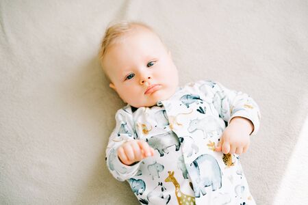 a small beautiful boy in a jumpsuit with animals is lying on the couch