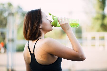 young attractive girl in sportswear on the Playground drinking water their sports bottle in the summerの写真素材