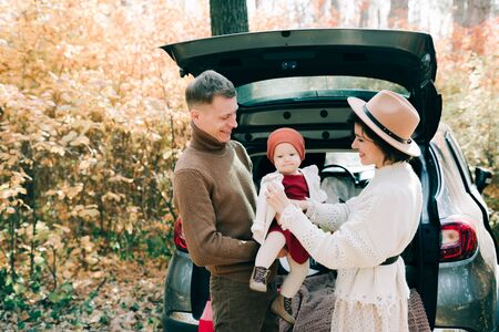 a happy family of four people in an autumn pine forest sit in the cozy trunk of their car covered with blankets. golden leavesの写真素材