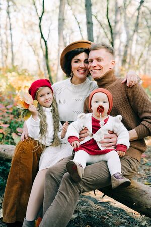 happy family of four sitting on a fallen tree in the middle of a pine forest in the autumn