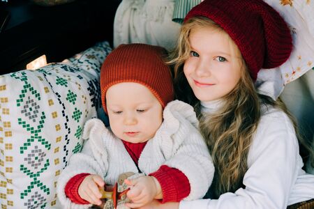 two beautiful little girls sit in the cozy trunk of a car in a pine forestの写真素材